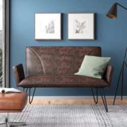 A brown leather sofa with a brown leather footrest is placed next to a high-rise window for a comfy aesthetic in an urban environment.