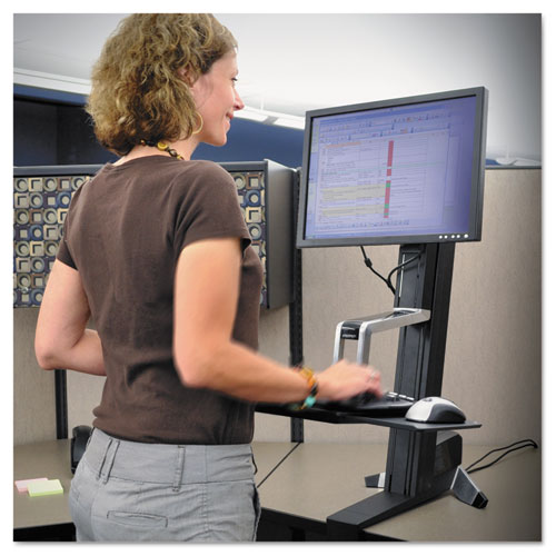 A woman works while standing with the help of a sit-stand workstation.