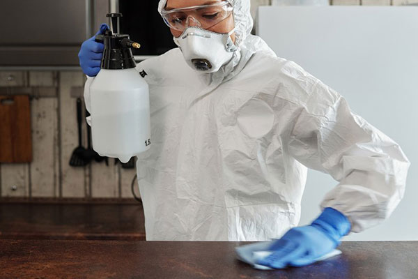 man in white, sterile suit disinfecting a table