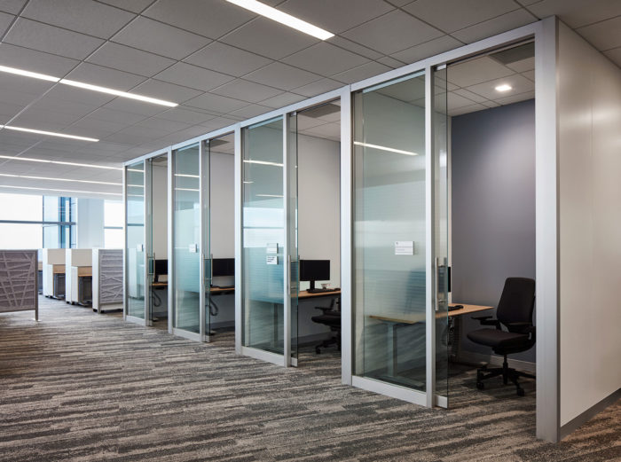 An open floor plan of an office with glass separators between each cubicle