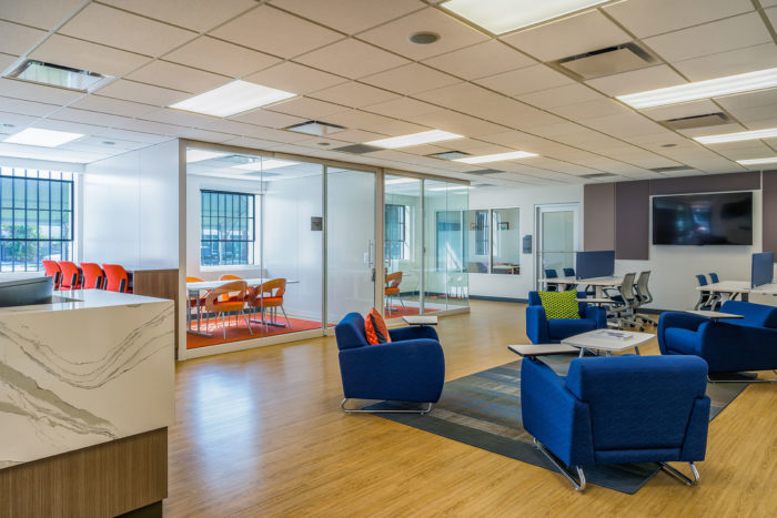 Lounge area of an office space with blue arm chairs overlooking offices with orange chairs